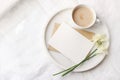 Breakfast in bed mockup scene near window. Cup of coffe, greeting card, narcissus, daffodil flowers on marble tray