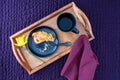 Breakfast in bed, partially eaten homemade cranberry scone on black plate and wood tray on a purple bedspread