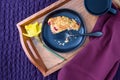 Breakfast in bed, partially eaten homemade cranberry scone on black plate and wood tray on a purple bedspread