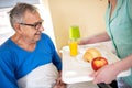 Breakfast in bed, residential care in a nursing home, elder man nursing home occupant being served breakfast by a nurse