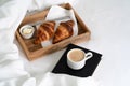 Breakfast in bed with two croissants and butter on the wooden tray, a cup of coffee and book on the white sheet with blanket. Royalty Free Stock Photo