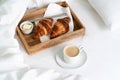 Breakfast in bed with two croissants and butter on the wooden tray, a cup of coffee on the white sheet. Royalty Free Stock Photo