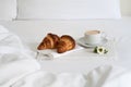 Breakfast in bed with two croissants and a cup of coffee with white flower on the marble tray. Royalty Free Stock Photo