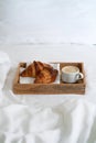 Breakfast in bed with two croissants and a cup of coffee on the wooden tray on the white sheet Royalty Free Stock Photo