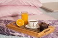 Breakfast in bed on a wooden tray with muffin, orange juice and coffee. Bed of purple tones. Horizontal position