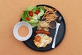 Breakfast in the black round plate on the brown floor. Fried egg with sausage, dumpling with french fries and vegetable with Royalty Free Stock Photo