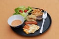 Breakfast in the black round plate on the brown floor. Fried egg with sausage, dumpling with french fries and vegetable with Royalty Free Stock Photo