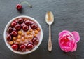 Breakfast bowl with yogurt, granola or muesli or oat flakes, fresh cherries and nuts. Black stone background, pink rose flower. T Royalty Free Stock Photo