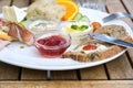 Breakfast with bread, butter and jam, also various cold cuts and fruits on a white plate on a wooden outdoor table, selected focus Royalty Free Stock Photo