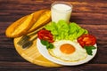 Breakfast with bread, fried eggs, milk and vegetables and fried tomato pieces on wood background. Royalty Free Stock Photo