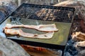 Breakfast camp cooking. Grilling crispy bacon on a cast iron plate over the camp fire