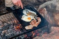 Breakfast camp cooking. Grilling crispy bacon and eggs on a cast iron plate over the camp fire Royalty Free Stock Photo