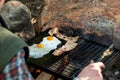 Breakfast camp cooking. Grilling crispy bacon and eggs on a cast iron plate over the camp fire