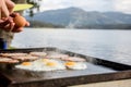 Breakfast camp cooking, Grilling eggs and bacon on the bbq plate with beautiful nature landscape