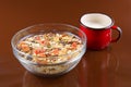 Breakfast cereals, oatmeal with candied fruits and nuts in a glass bowl and red cup milk, brown background Royalty Free Stock Photo