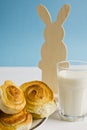 Breakfast with cinnamon buns and glass of milk on a blue background with decoration Easter bunny. Royalty Free Stock Photo