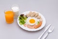 Breakfast consists of fried egg, ham, sausage, milk, orange, whole wheat bread shaped like a heart, fresh vegetables, put plates