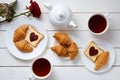 Breakfast for couple on Valentines Day with toasts, heart shaped jam, croissants, red rose flower and tea, white wooden Royalty Free Stock Photo