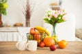 Breakfast cups and fruit. Spring tulips on the table. Wooden table in a bright rustic-style kitchen. Scandinavian style in the int