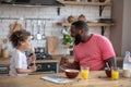 Cute kid with curly hair and her father holding spoons as microphones and singing before having breakfast