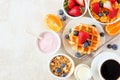 Breakfast table scene with fruits, cereal, waffles, yogurt and coffee. Top view over a bright stone background. Royalty Free Stock Photo