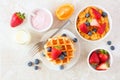 Breakfast table scene with fruits, cereal, waffles, yogurt and milk. Top view over a bright background. Royalty Free Stock Photo