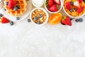 Breakfast top border of fruits, cereal, waffles and milk. Top view over a bright stone background.