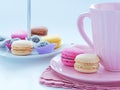 Breakfast with French macarons and a cup of cocoa in pink porcelain mug. Assortment of small cookies in the background