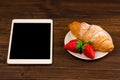 Breakfast with fresh croissants, fresh strawberry on a rustic wooden background, top view. tablet pc.