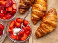 Breakfast with fresh croissants, strawberry with cream in glass bowls background