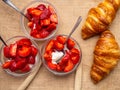 Breakfast with fresh croissants, strawberry with cream in glass bowls background