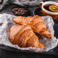 Breakfast with fresh french chocolate croissants on paper over dark background with napkin and cup of tea. Dessert, puff pastries Royalty Free Stock Photo