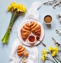 Breakfast with fresh French croissants, jam and coffee with spring flowers bouquet of daffodils on a light blue Royalty Free Stock Photo