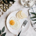 Breakfast of fried egg and pear on a white plate with a fork. In a glass bowl, yogurt and a dragon fruit, next to a tray of quail