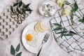 Breakfast of fried egg and pear on a white plate with a fork. In a glass bowl, yogurt and a dragon fruit, next to a tray of quail