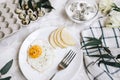 Breakfast of fried egg and pear on a white plate with a fork. In a glass bowl, yogurt and a dragon fruit, next to a tray of quail