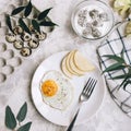 Breakfast of fried egg and pear on a white plate with a fork. In a glass bowl, yogurt and a dragon fruit, next to a tray of quail