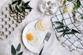 Breakfast of fried egg and pear on a white plate with a fork. In a glass bowl, yogurt and a dragon fruit, next to a tray of quail