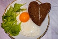 Breakfast with fried egg, slices bread with heard shape and greenery on white plate Royalty Free Stock Photo