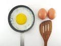 fried egg in teflon pan, two raw eggs and wooden spatula isolated on white background Royalty Free Stock Photo