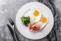 Breakfast, fried eggs, bacon, prosciutto, fresh salad on plate on grey table surface. Healthy food, top view, flat lay