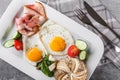 Breakfast, fried eggs, bun, bacon, prosciutto, fresh salad on plate on grey table surface