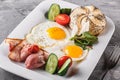 Breakfast, fried eggs, bun, bacon, prosciutto, fresh salad on plate on grey table surface