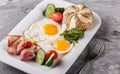 Breakfast, fried eggs, bun, bacon, prosciutto, fresh salad on plate on grey table surface. Healthy food, top view, flat lay Royalty Free Stock Photo