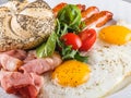Breakfast, fried eggs, bun, sausage, bacon, prosciutto, fresh salad on plate on grey table surface. Healthy food Royalty Free Stock Photo