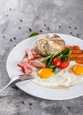 Breakfast, fried eggs, bun, sausage, bacon, prosciutto, fresh salad on plate on grey table surface. Healthy food, top view Royalty Free Stock Photo