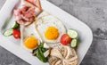 Breakfast, fried eggs, bun, sausage, bacon, prosciutto, fresh salad on plate on grey table surface. Healthy food, top view, flat