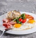 Breakfast, fried eggs, bun, sausage, bacon, prosciutto, fresh salad on plate on grey table surface. Healthy food, top view, flat Royalty Free Stock Photo
