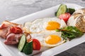 Breakfast, fried eggs, bun, sausage, bacon, prosciutto, fresh salad on plate on grey table surface. Healthy food, top view, flat Royalty Free Stock Photo