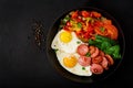 Fried eggs with sausage and vegetables in a frying pan on a black background in rustic style Royalty Free Stock Photo